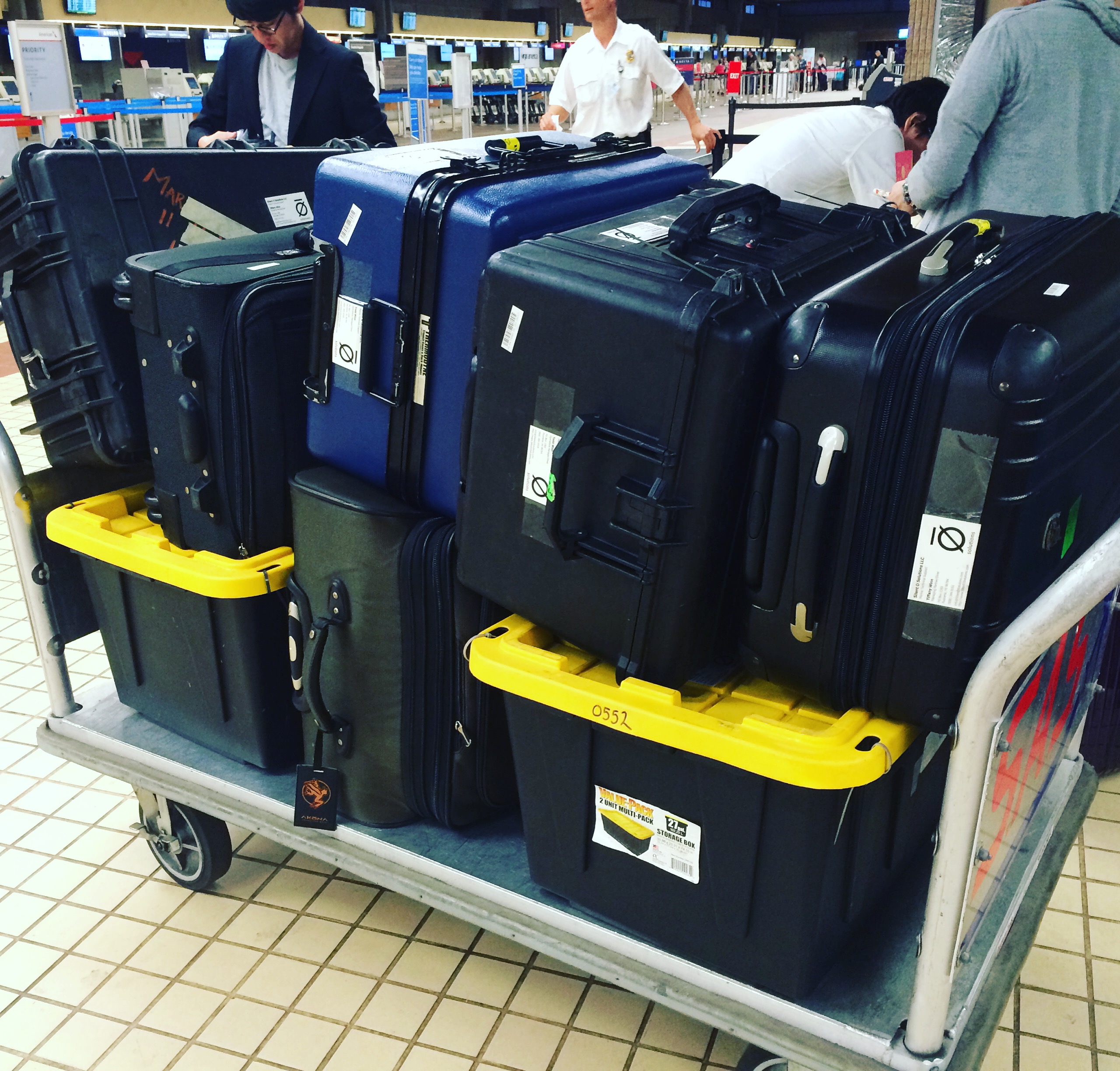 Airport luggage cart stacked with hard equipment cases.